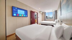 Een hotelkamer met een groot bed, een kleiner bed, een aan de muur bevestigde televisie en een raam met uitzicht op de stad.