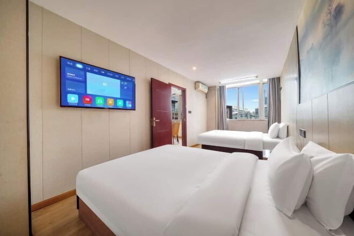 Quarto de hotel com uma cama grande, uma cama menor, uma TV fixada na parede e uma janela com vista para a cidade.