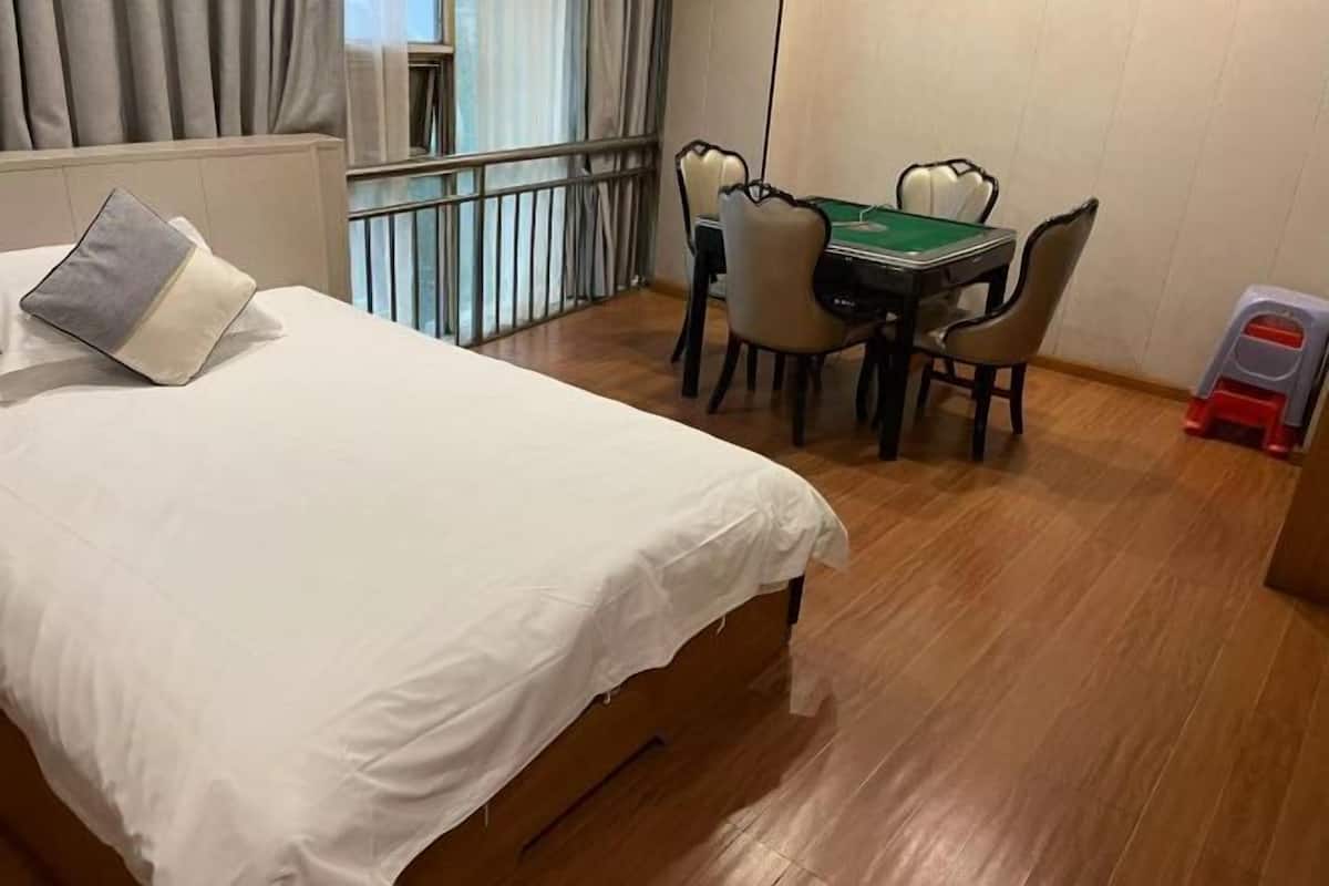 Quarto de hotel com uma cama, uma mesa de jantar com cadeiras e um banquinho.