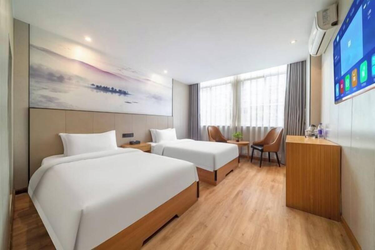 Quarto de hotel com duas camas, uma escrivaninha, uma cadeira, uma televisão e uma janela grande.