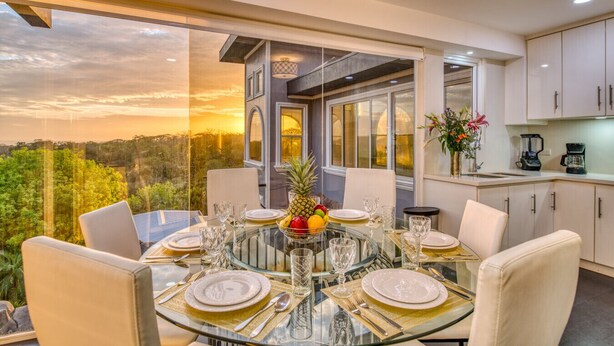A dining area with a glass table set for six, overlooking a scenic view.