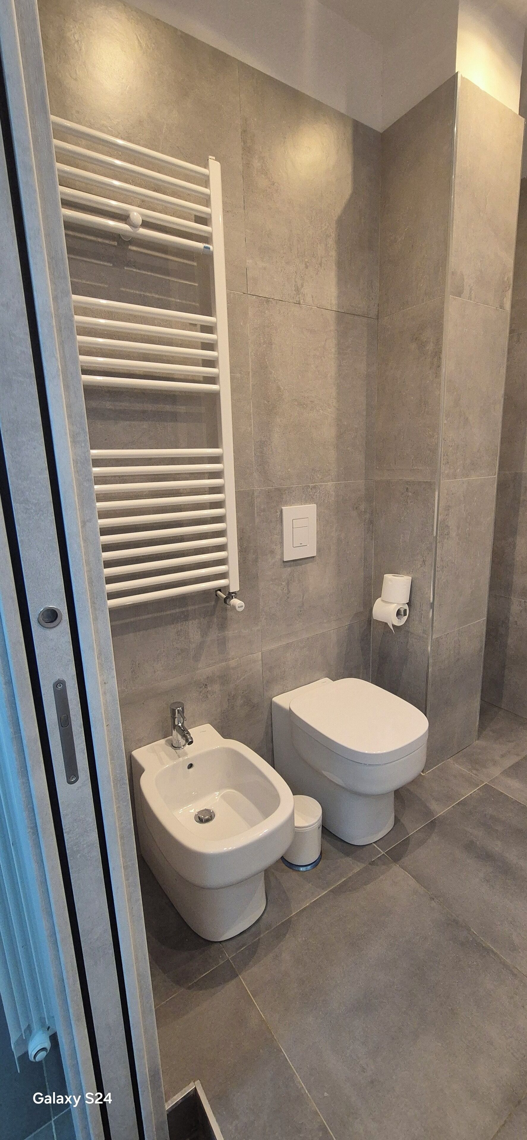 Een moderne badkamer met een toilet, handdoekrek en een hygiëneschuimer.