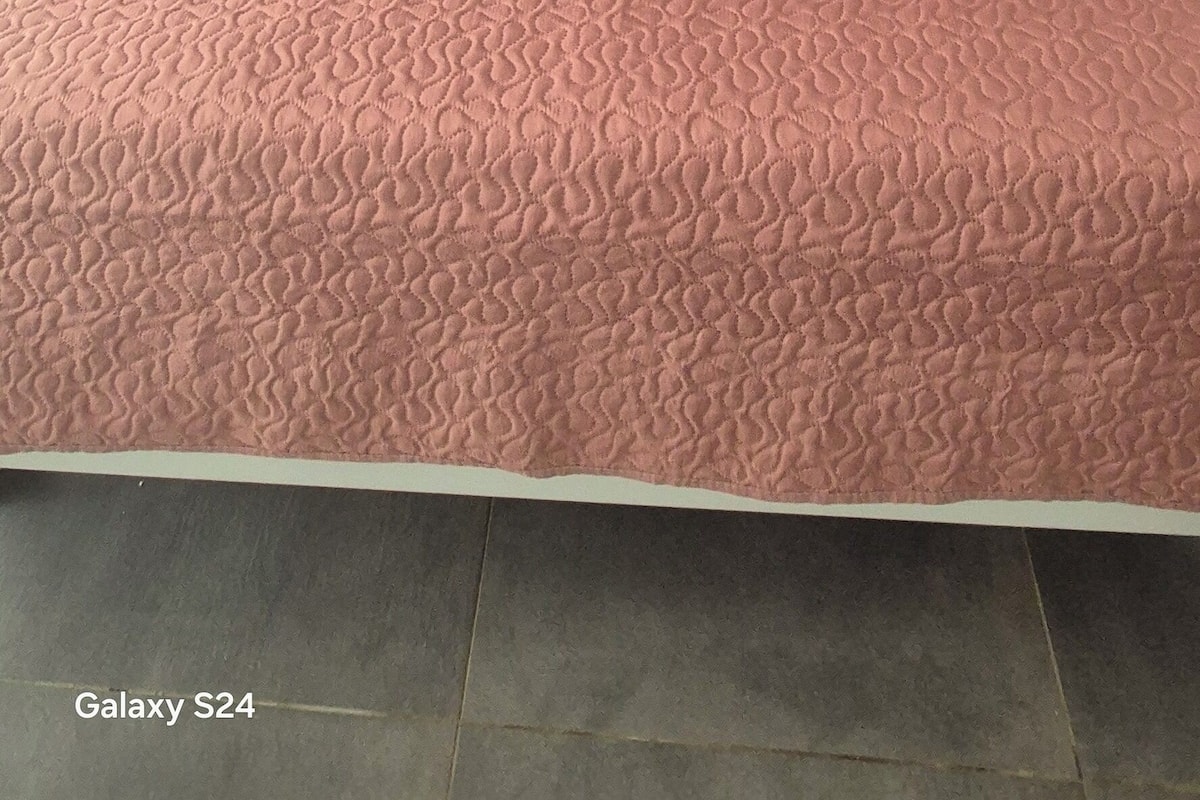 A bed with a pink quilt, a white headboard, and a wall decoration above it.
