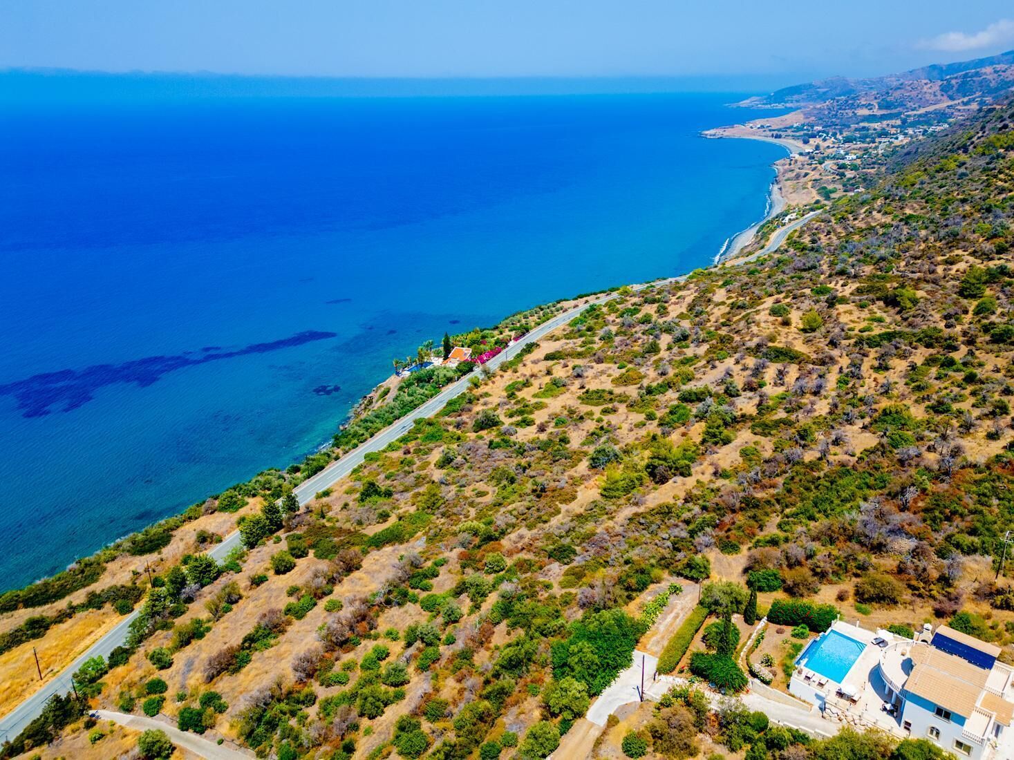 An aerial view of a coastal property with a road leading to a house with a swimming pool.