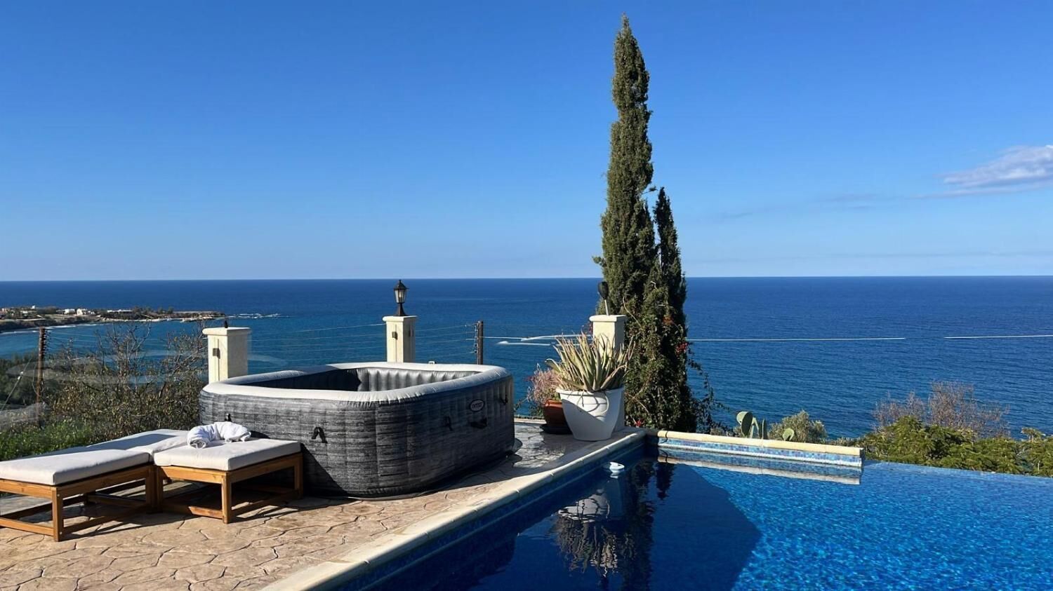 An infinity pool with a view of the sea, lounge chairs, and a tall tree.