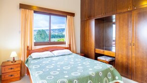 Un dormitorio con cama, mesita de noche, armario y ventana con cortinas.
