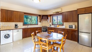 Una cocina moderna con armarios de madera, un refrigerador de acero inoxidable, un horno empotrado y una mesa de comedor con sillas.