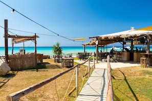 A beachside restaurant with outdoor seating, a wooden deck, and a view of the ocean.