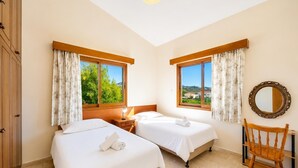 Une chambre d’hôtel avec deux lits, une chaise en bois, un miroir et une vue sur la verdure et les bâtiments.