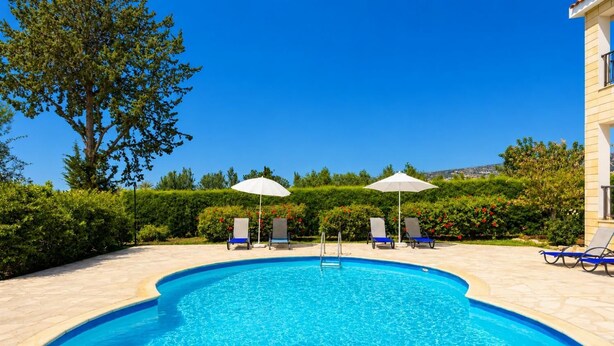 Une piscine entourée de verdure et d’un bâtiment, avec des chaises longues et des parasols.