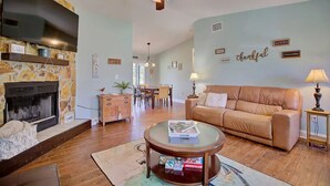 Una sala de estar acogedora con chimenea, un sofá de cuero, una zona de comedor y un ventilador de techo.