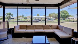 Un área de estar al aire libre cubierta con un sofá, una mesa, ventanas amplias y un ventilador de techo.