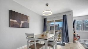 Zona pranzo con tavolo e sedie, una lampada a sospensione, una finestra con tende e vista all'esterno.