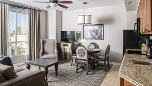 A modern living room with a flat-screen TV, a dining area with a table and chairs, a ceiling fan, and a kitchen with granite countertops. - Grand Desert 1 Bedroom Suite, Las Vegas! (Las Vegas)