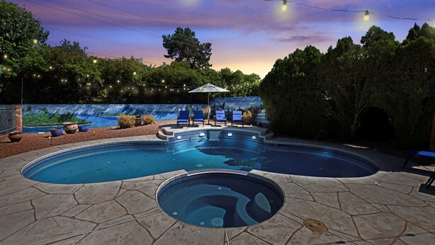 Una piscina con hidromasaje, rodeada de baldosas de piedra, y una zona de estar con sillas y una sombrilla.
