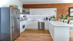 A modern kitchen with white cabinets, stainless steel appliances, a brick accent wall, and a wooden floor.