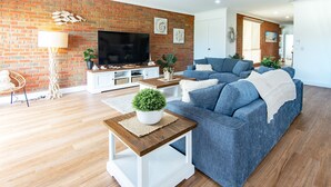 A modern living room with a brick wall, a flat-screen TV, a blue sofa, and a wooden coffee table.