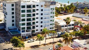 A multi-story hotel with a pool on the ground floor, surrounded by palm trees and a view of the sea. - New Centric apt. with pool & jacuzzi (Mazatlán)