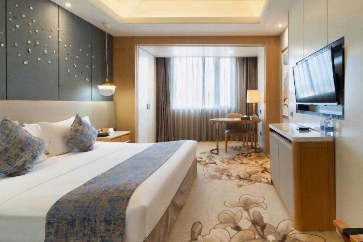 A hotel room with a bed, a desk, a television, and a bathroom visible through a door.