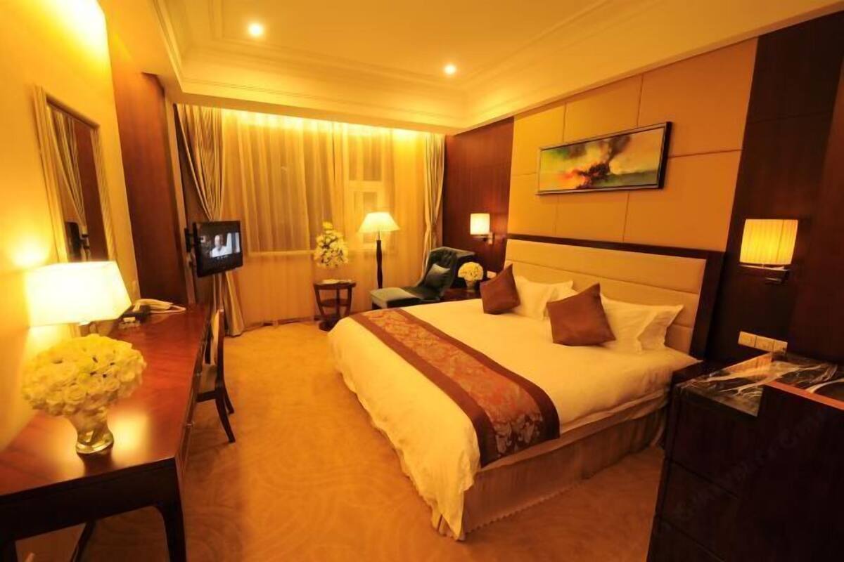A hotel room with a large bed, a desk with a lamp, a television, and a painting on the wall.
