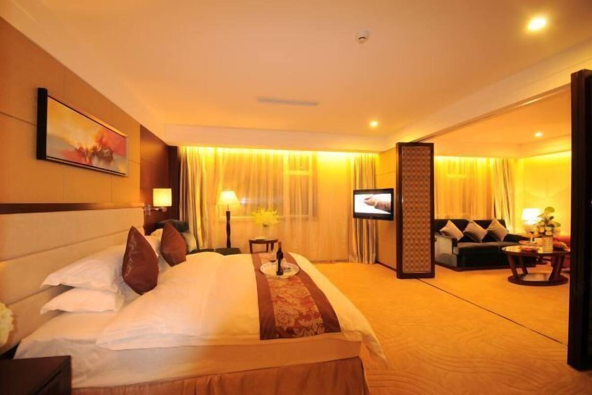 A hotel room with a bed, a TV, a sofa, and a dining table.