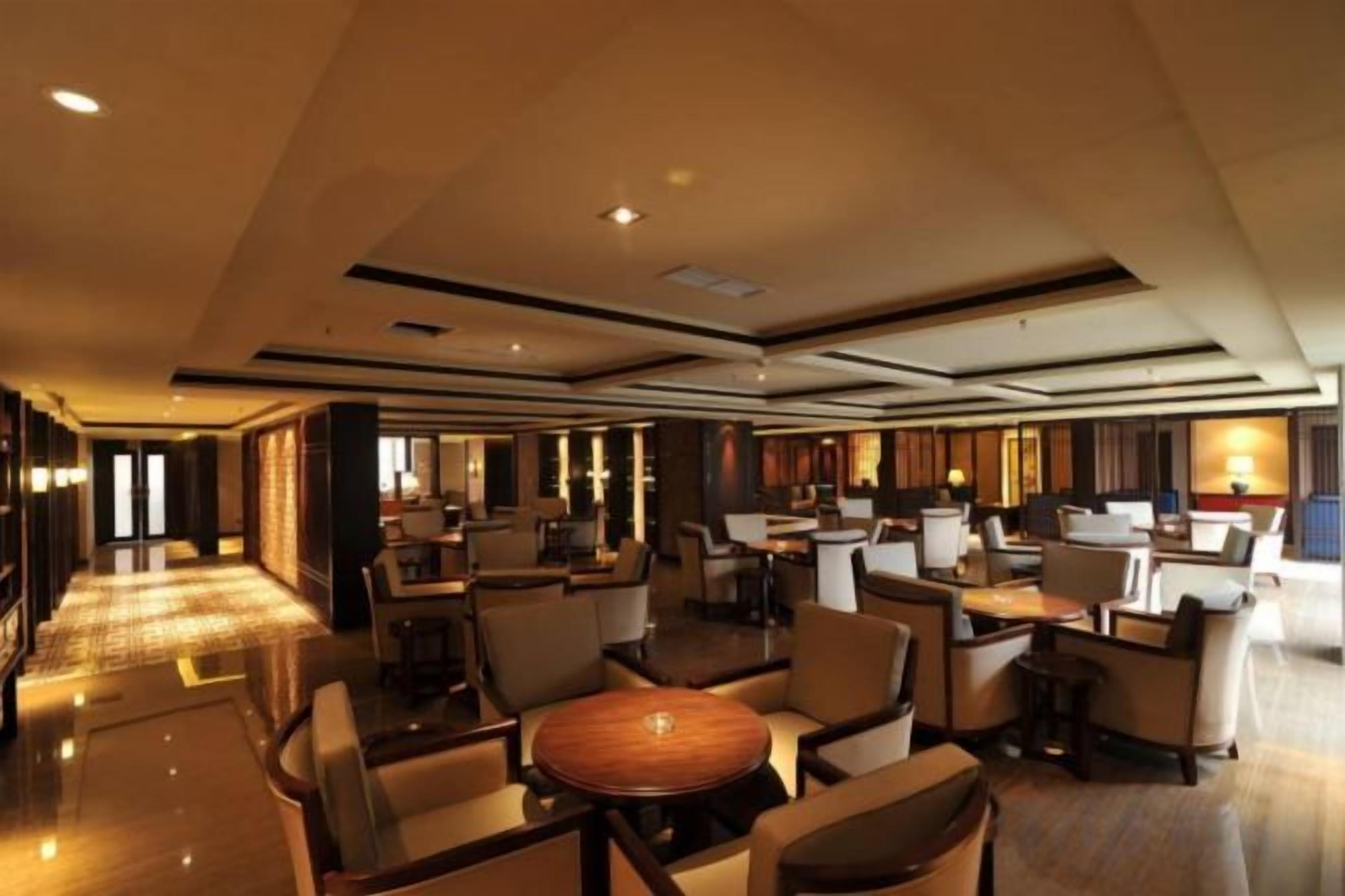 A spacious hotel lobby with multiple seating areas, a reception desk, and a well-lit environment.