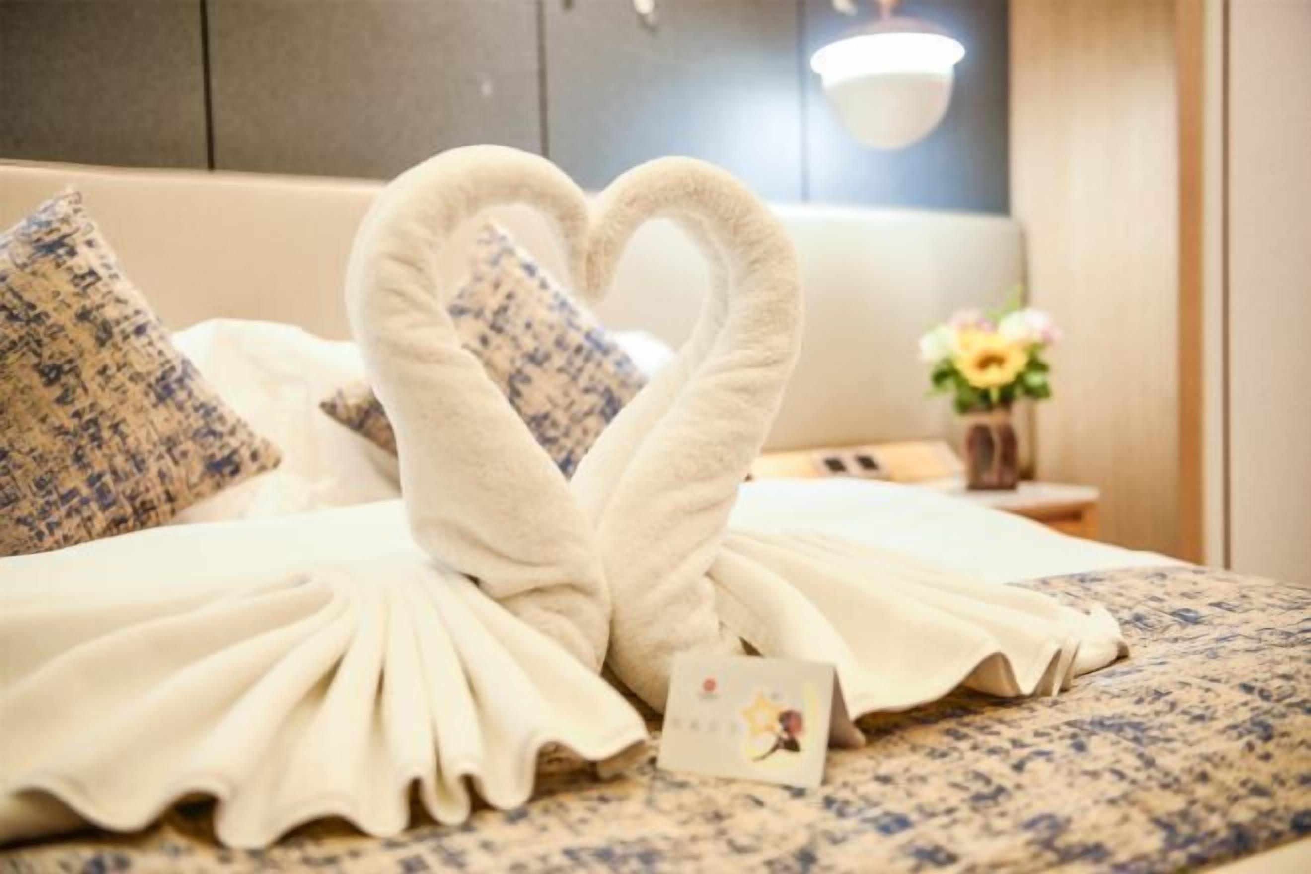 A bed with a heart-shaped towel arrangement and a card on the bed.