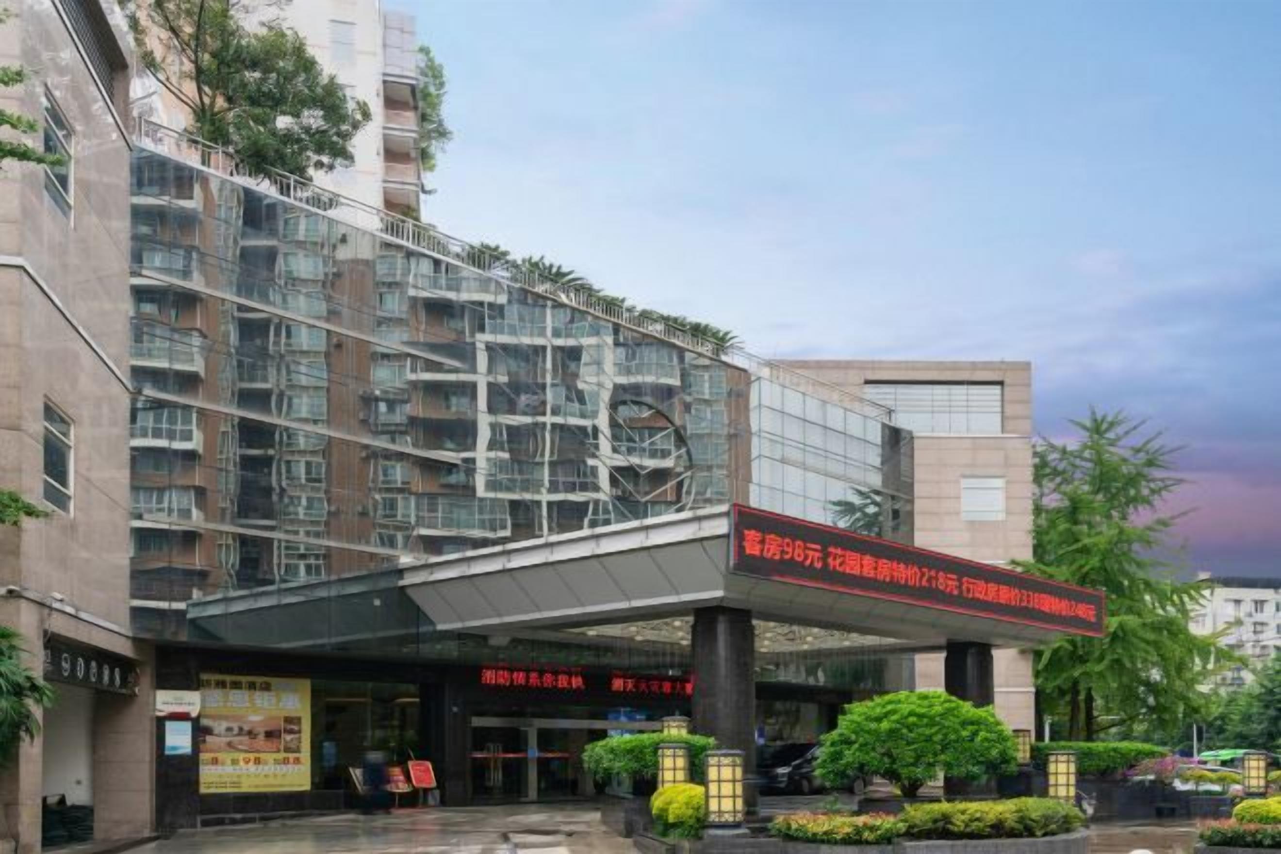 A multi-story building with a covered entrance, signage, and a landscaped area with bushes.