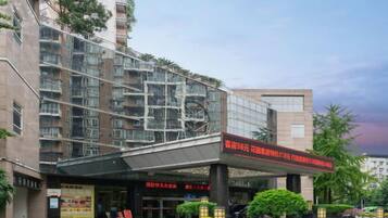 A multi-story building with a covered entrance, signage, and a landscaped area with bushes.