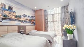 Habitación de hotel con dos camas, un mural de un paisaje urbano, un jarrón de flores y una ventana con cortinas.