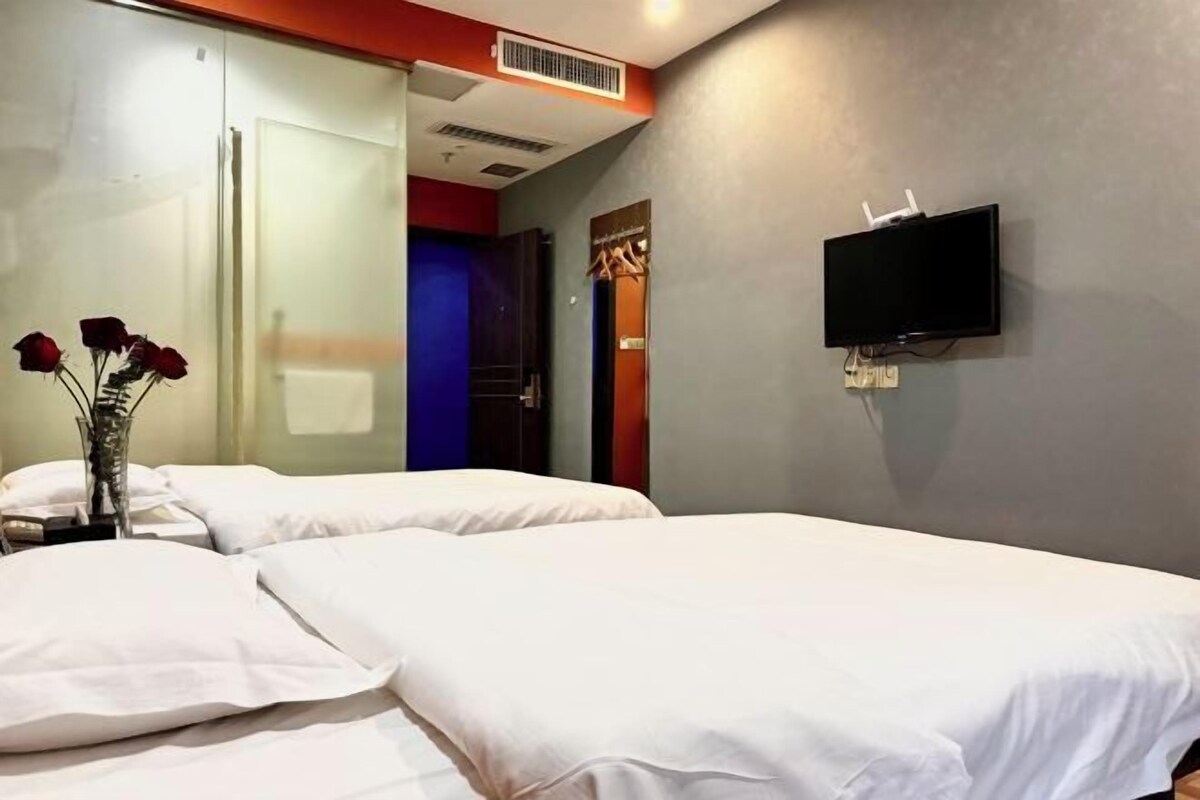 A hotel room with two beds, a flat-screen TV mounted on the wall, and a vase with red roses on the nightstand.