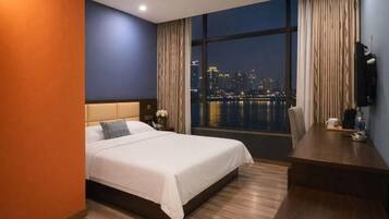 Habitación de hotel con cama, escritorio y vista a un paisaje urbano nocturno, además de un ventanal grande.