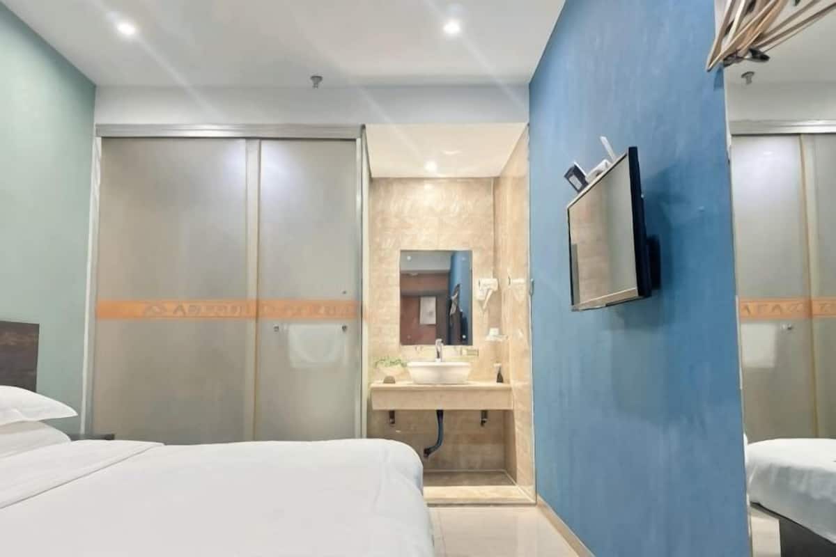 Une chambre d’hôtel comprenant un lit, une salle de bain avec un lavabo et un miroir, et un téléviseur fixé au mur.