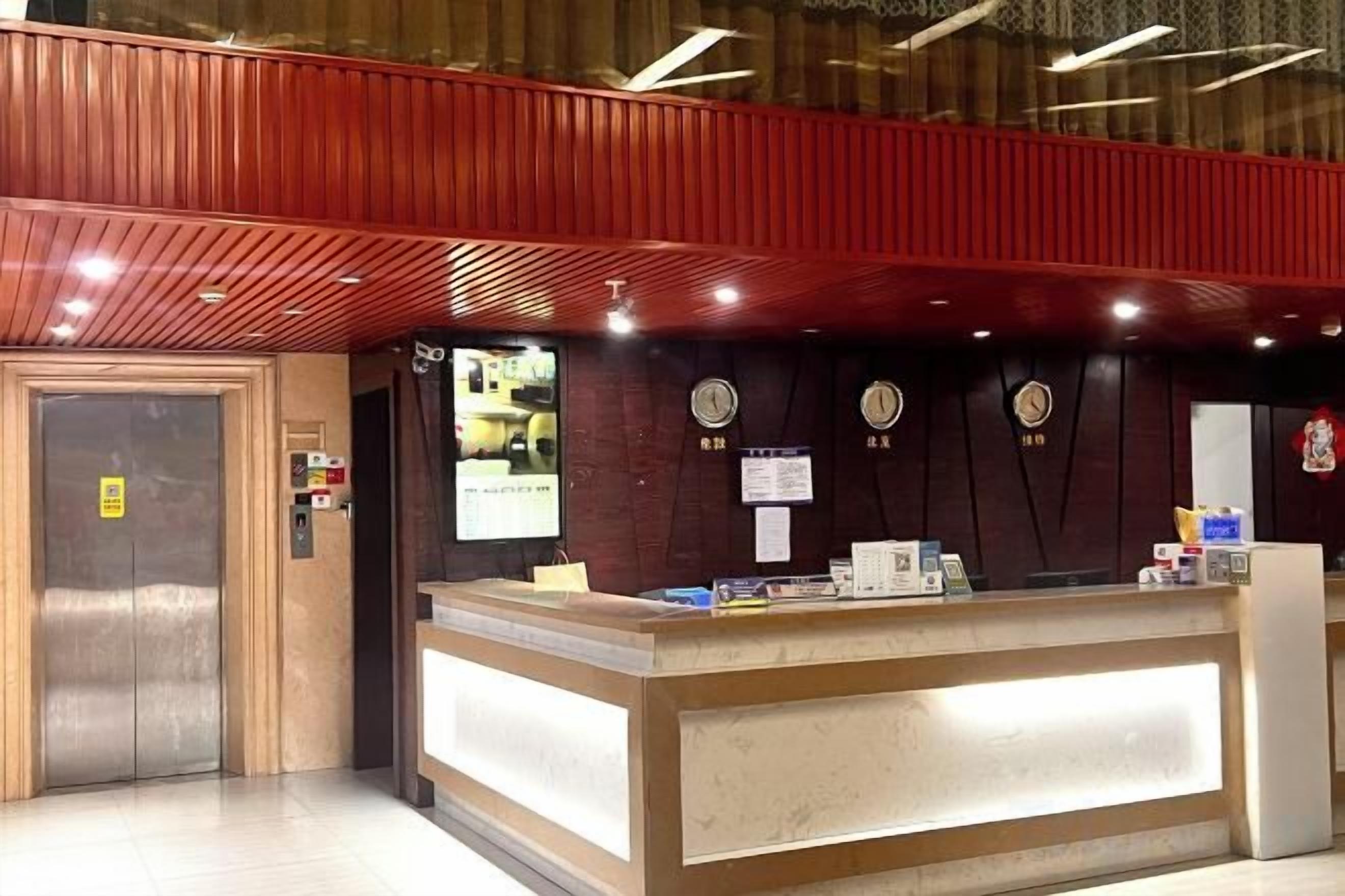 A hotel reception area with a wooden reception desk, a clock, and a fire alarm on the wall.