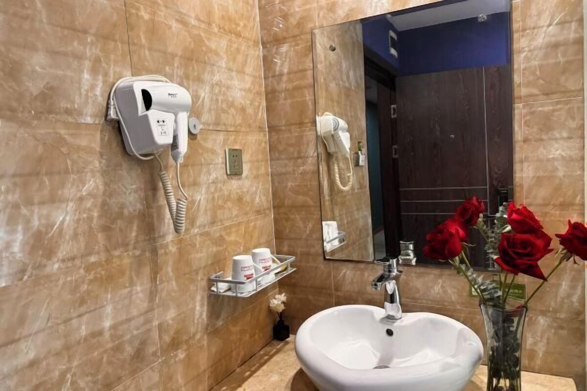 A bathroom with a white sink, a hairdryer, a mirror, and a vase with red roses.