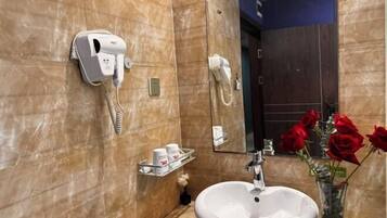 Un baño con un lavamanos blanco, un secador de pelo, un espejo y un florero con rosas rojas.