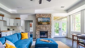 A spacious living room with a stone fireplace, a blue sofa, and a dining area with a table and chairs. - Lake retreat with unique dome near Indiana Dunes (Valparaiso)