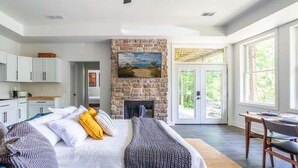 A bedroom with a stone fireplace, a bed with blue and white bedding, a desk with a chair, and a view of greenery through large windows. - Lake retreat with unique dome near Indiana Dunes (Valparaiso)