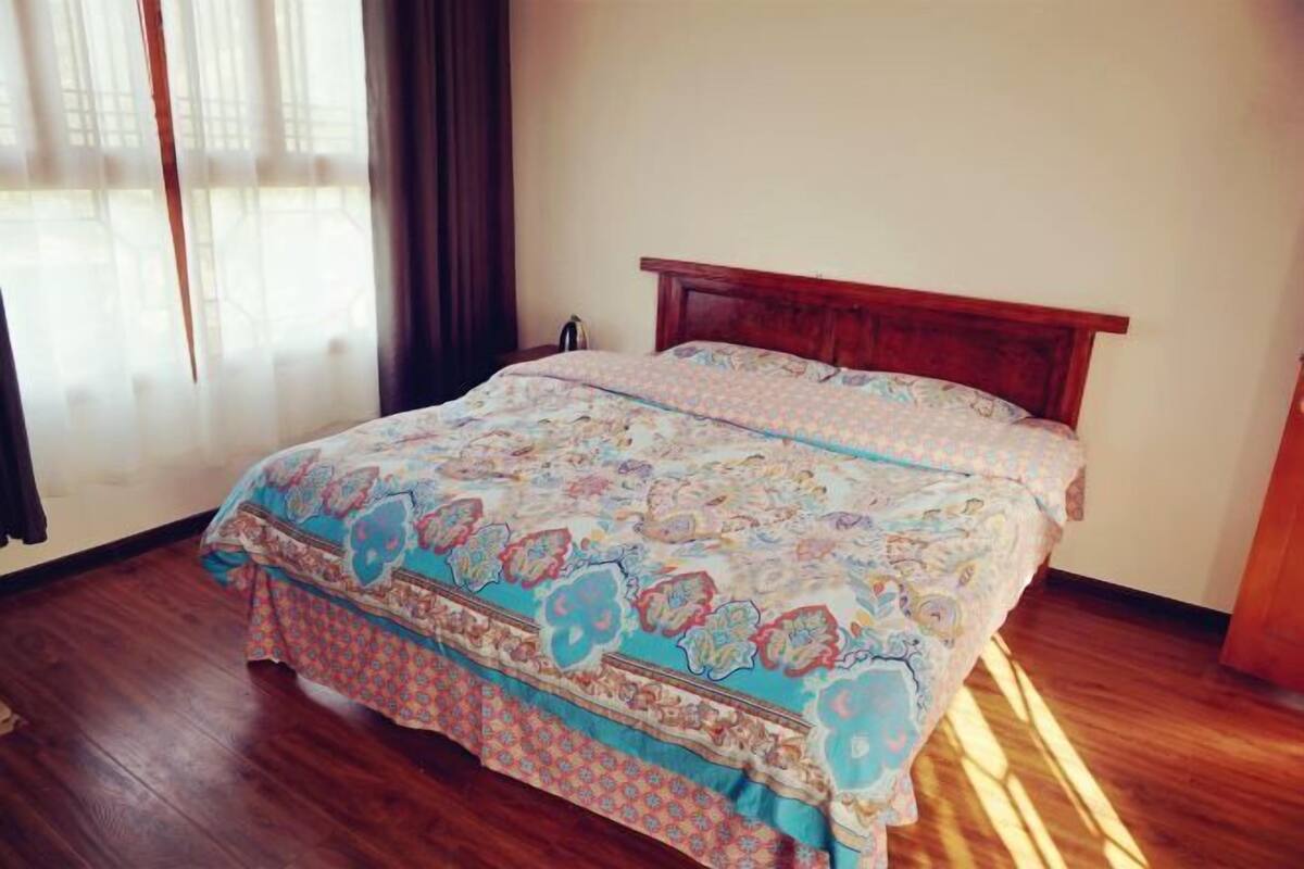 Quarto com estrutura de cama de madeira, colcha estampada e janela com cortinas.