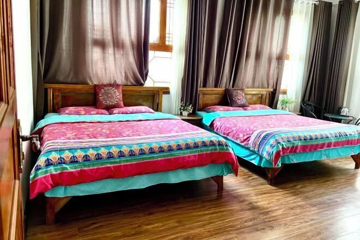 Duas camas de madeira com roupa de cama colorida, piso de madeira e uma janela com cortinas.