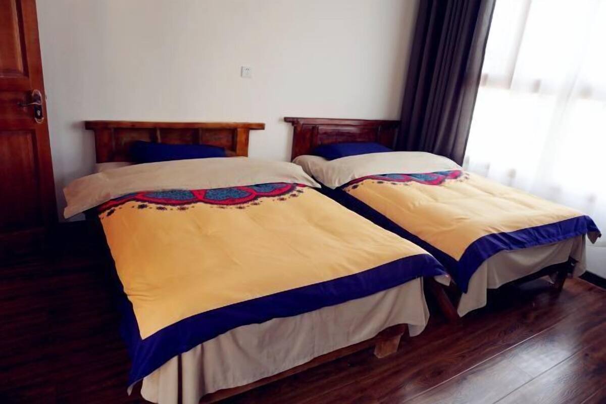 Duas camas de solteiro com cabeceiras de madeira, roupa de cama bege e azul, e piso de madeira.