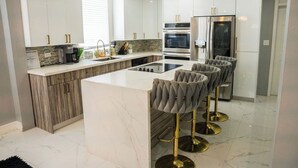 A modern kitchen with white cabinets, a marble island, and a built-in oven.