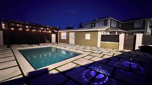 A swimming pool with a tiled deck and a pergola with string lights.