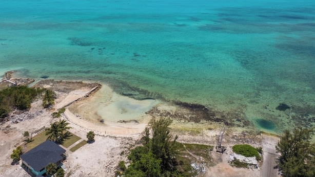 An aerial view of a coastal area with clear turquoise waters, sandy beach, and sparse vegetation.