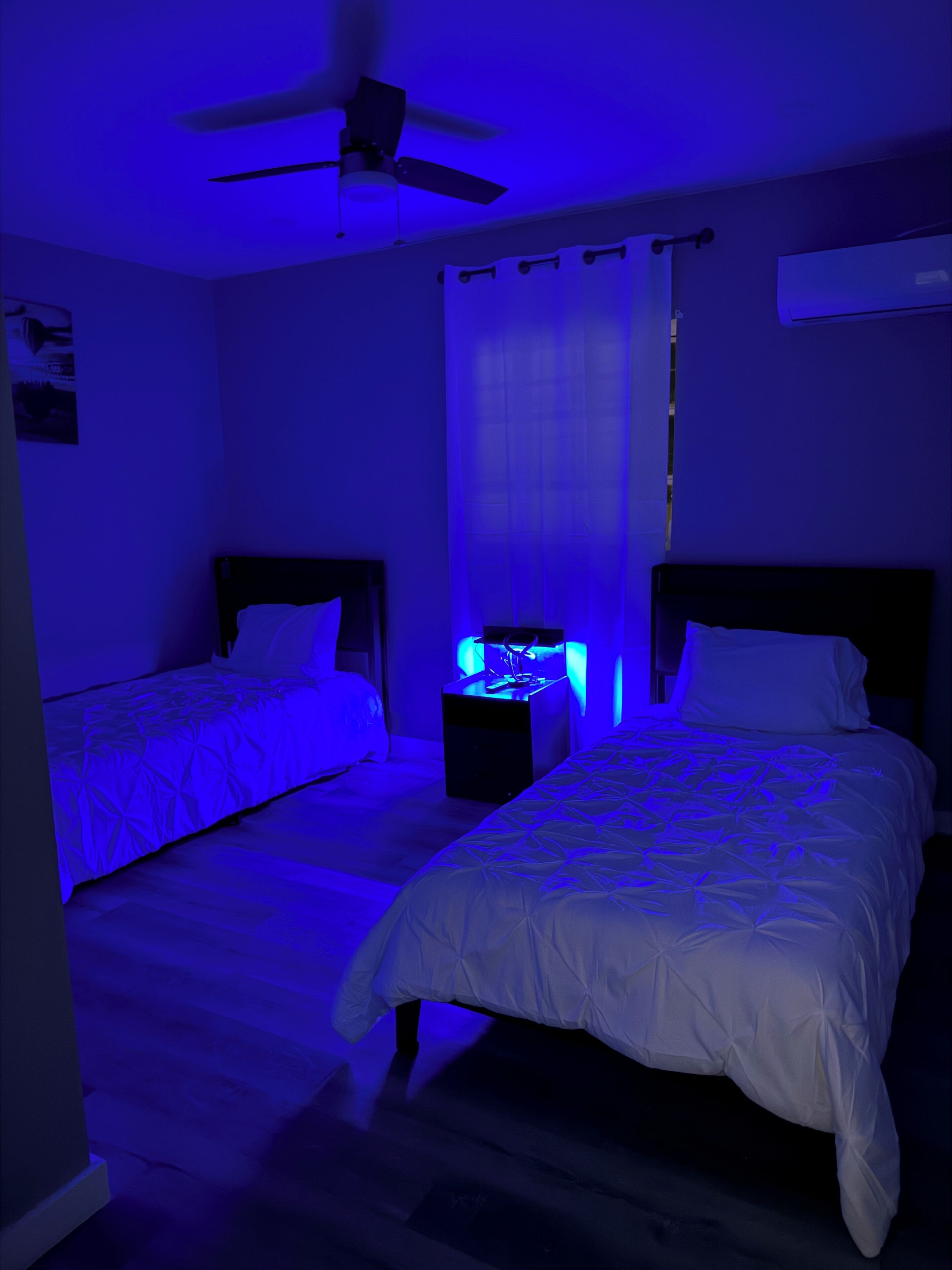Une chambre avec deux lits, un ventilateur de plafond et une table de chevet avec une lampe.