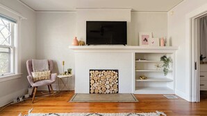 Una sala de estar con chimenea, un televisor montado encima y un sillón con cojín.