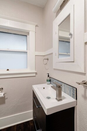 A bathroom with a white sink, a mirror, a window, and a towel rack. - Large SE Apartment • Walk to Eats • 1BR • Sleeps 4 (Portland)