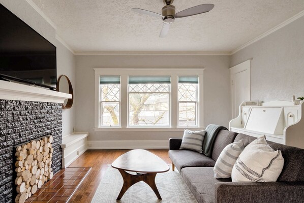 A living room with a fireplace, a sofa, a coffee table, and a TV mounted on the wall. - Large SE Apartment • Walk to Eats • 1BR • Sleeps 4 (Portland)
