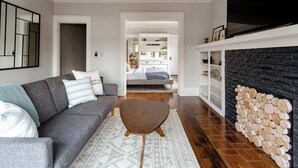 Un salon moderne avec un canapé gris, un tapis à motifs, une cheminée avec des bûches et un téléviseur fixé au-dessus.