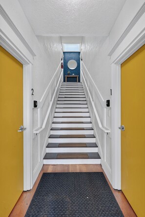 A staircase with white railings leading to a landing with a blue wall and a circular window.